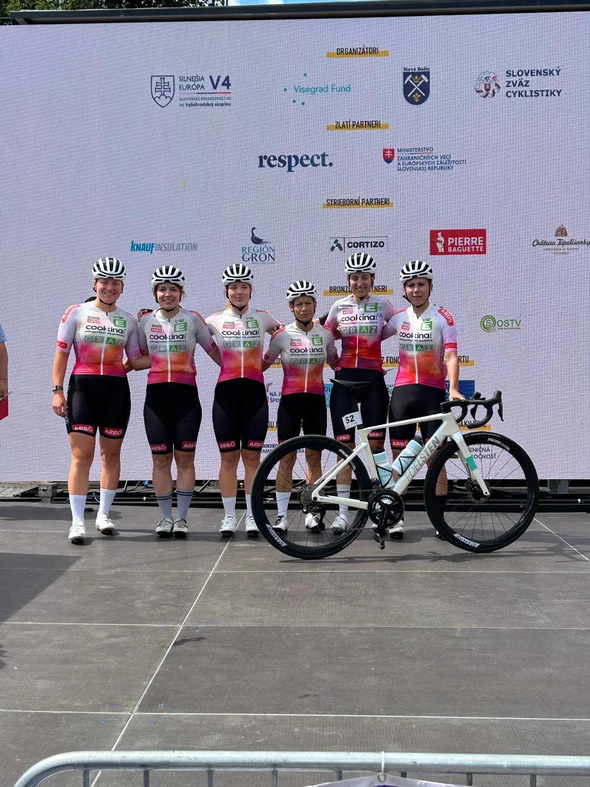 Six Cookina riders in their custom kit with a bike in front of the sponsor wall